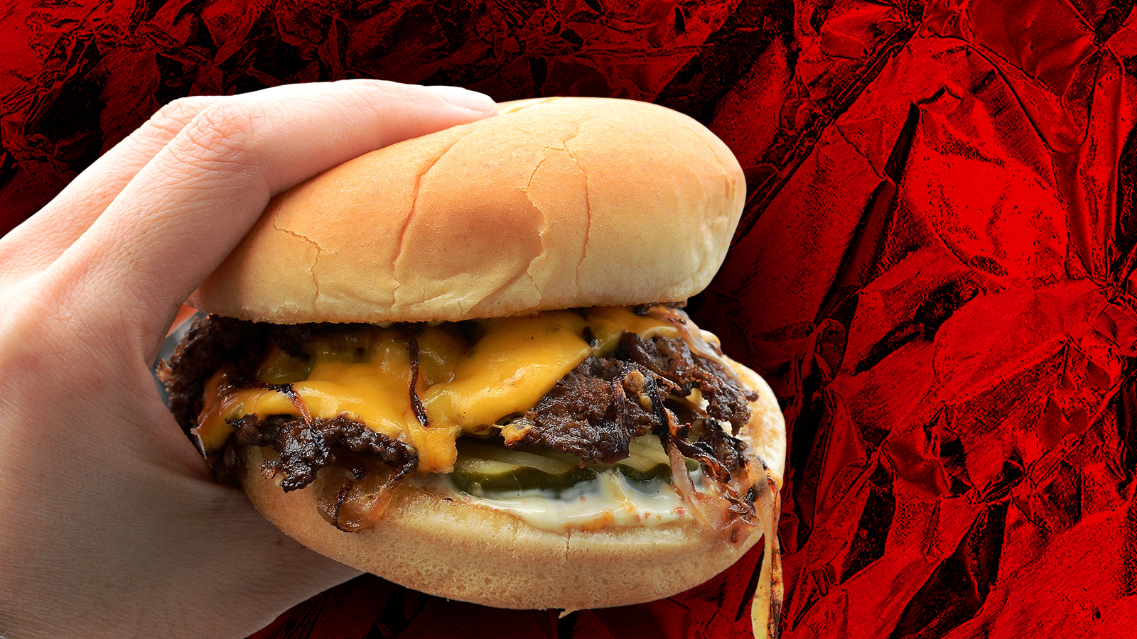 A hand holds a smash burger.