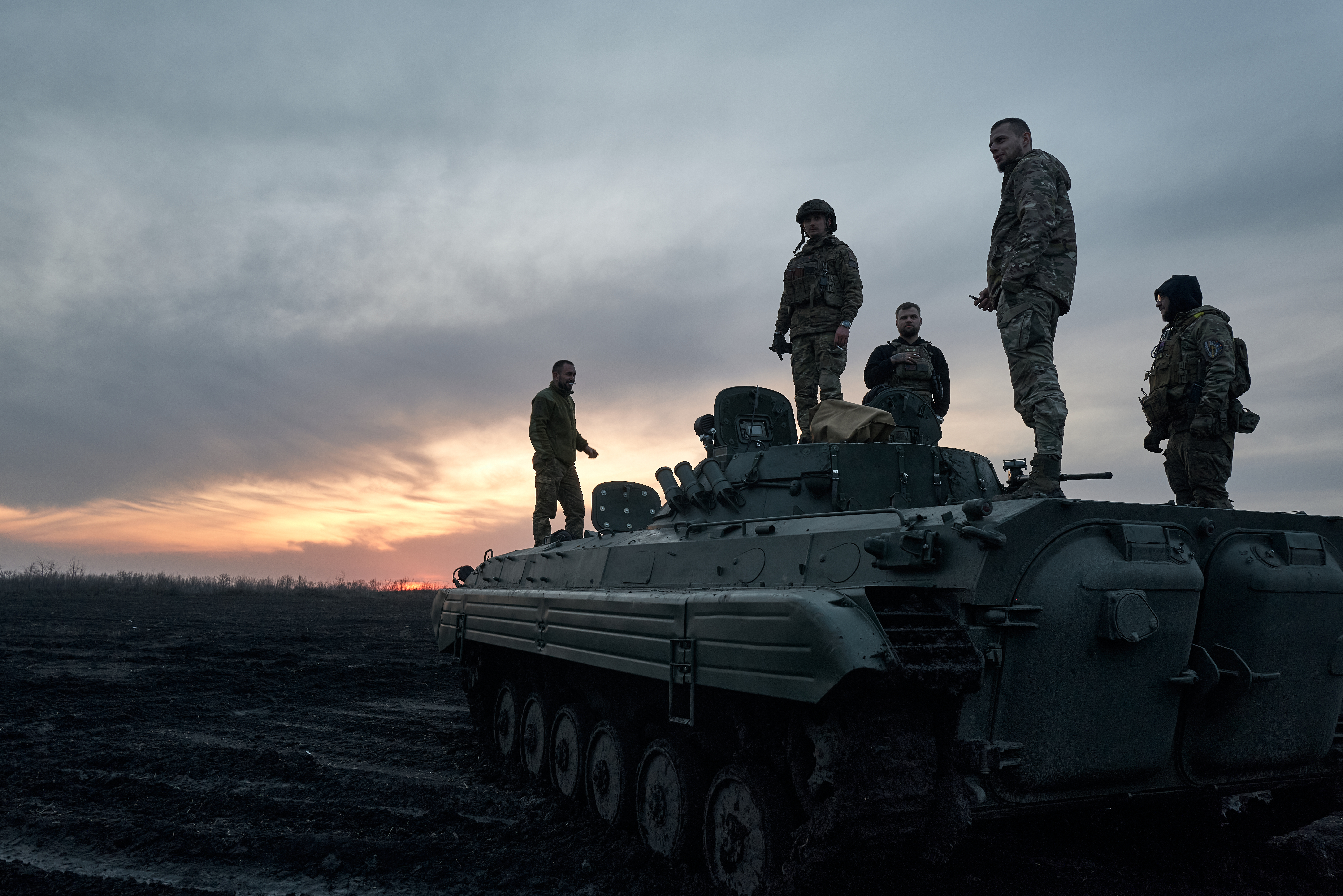 Soldiers standing on a tank in the sunset.