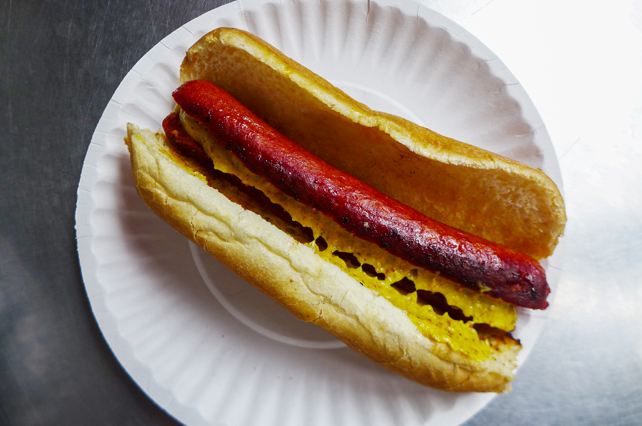 A hot dog with yellow mustard and a bun.