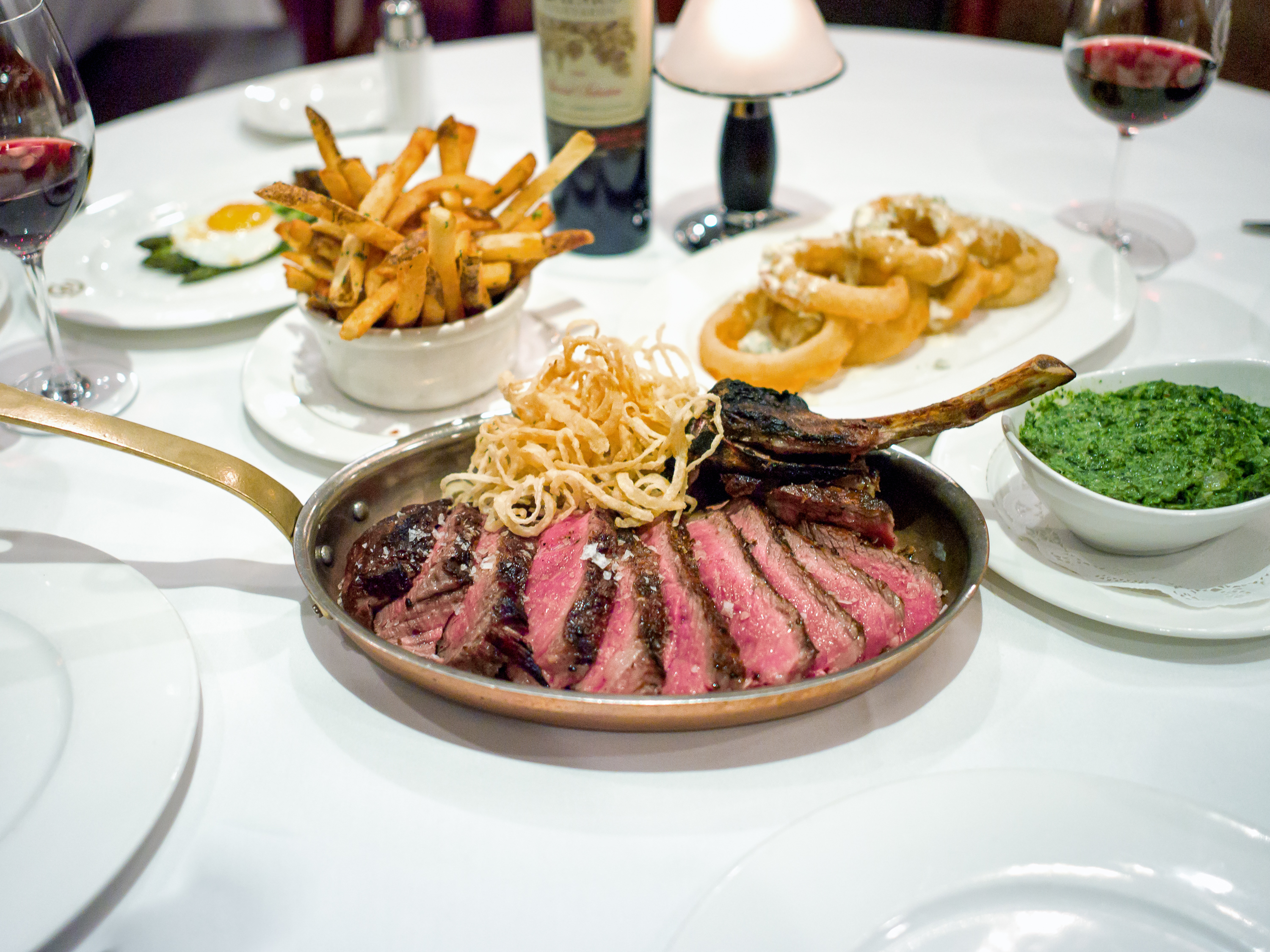 A steak on a crowded table with creamed spinach and french fries at Delmonico’s.