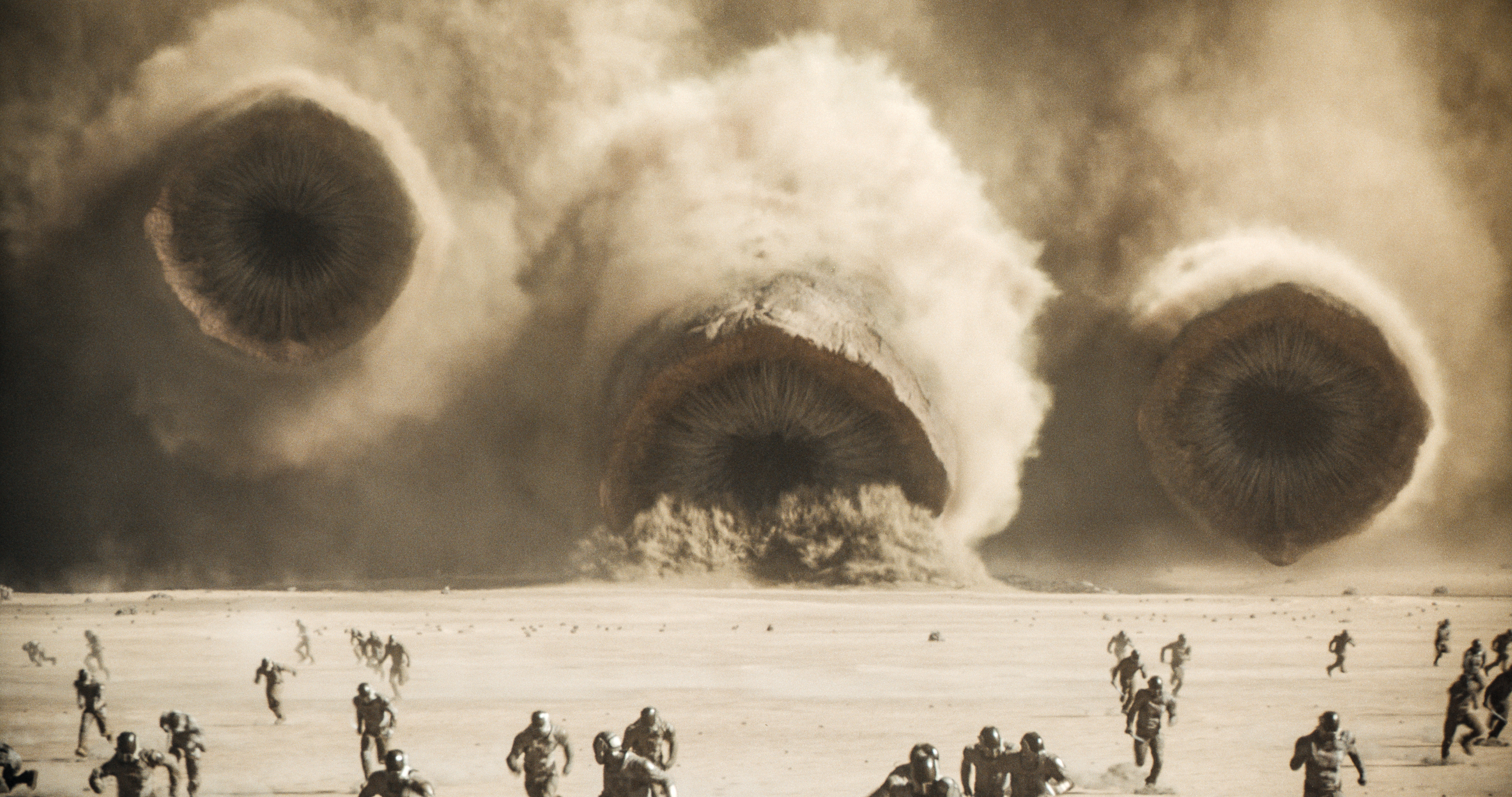People run from massive sandworms in a still from Dune. 