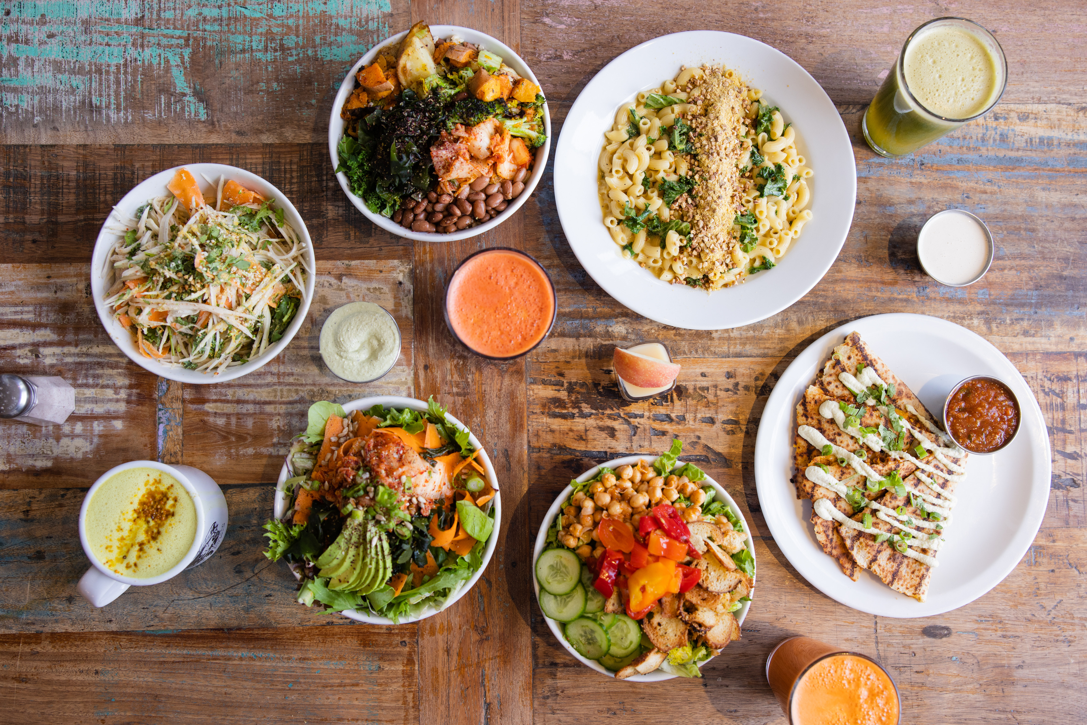 An overhead shot of a table with several dishes, including salads, a quesadilla, and mac and cheese.